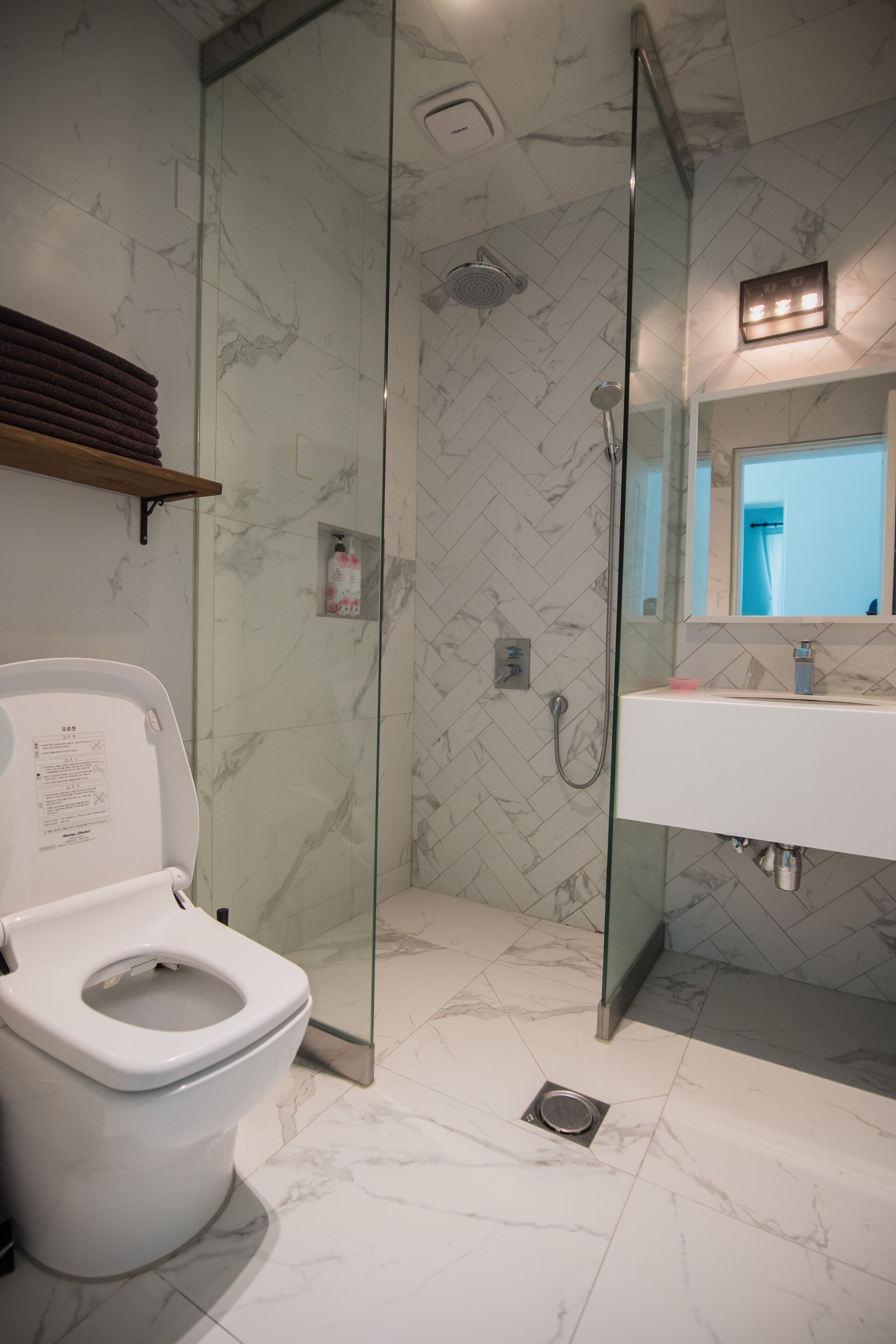 A modern bathroom with a glass-enclosed shower, a white toilet, and a sink with a mirror above it.