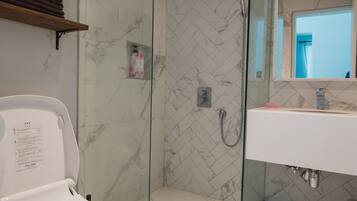 A modern bathroom with a glass-enclosed shower, a white toilet, and a sink with a mirror above it.