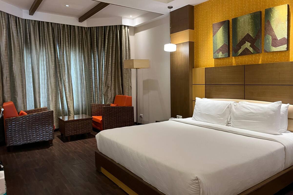 A hotel room with a large bed, a seating area with chairs, and a wall with three artworks.