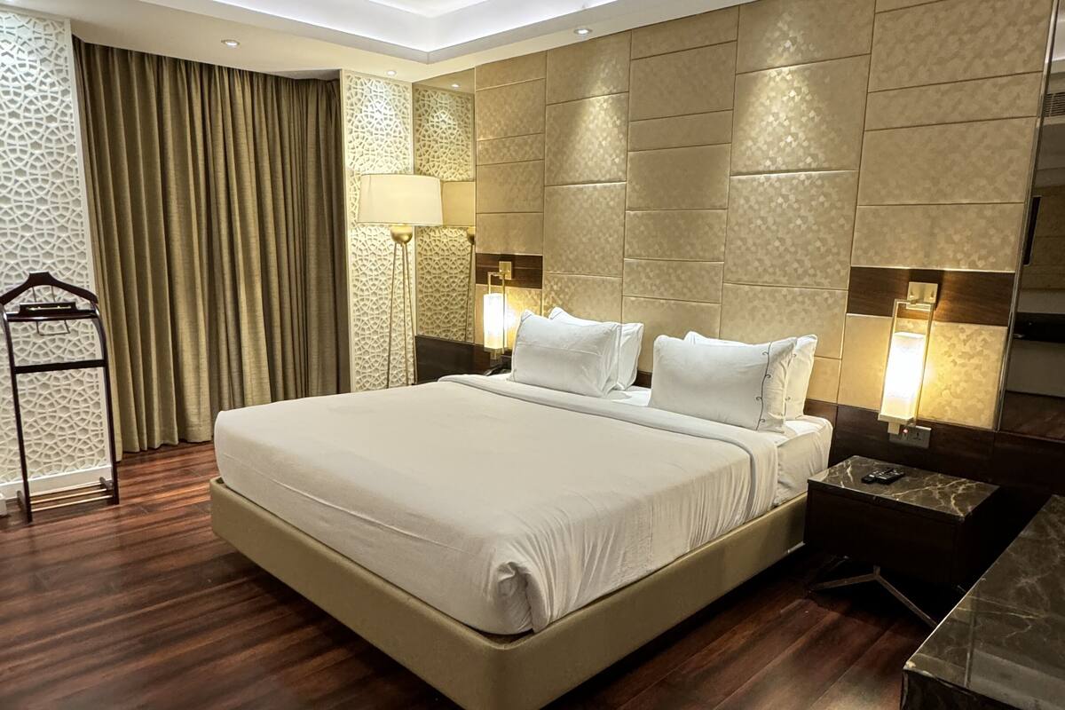 A modern hotel room with a large bed, wooden flooring, and a decorative wall panel.