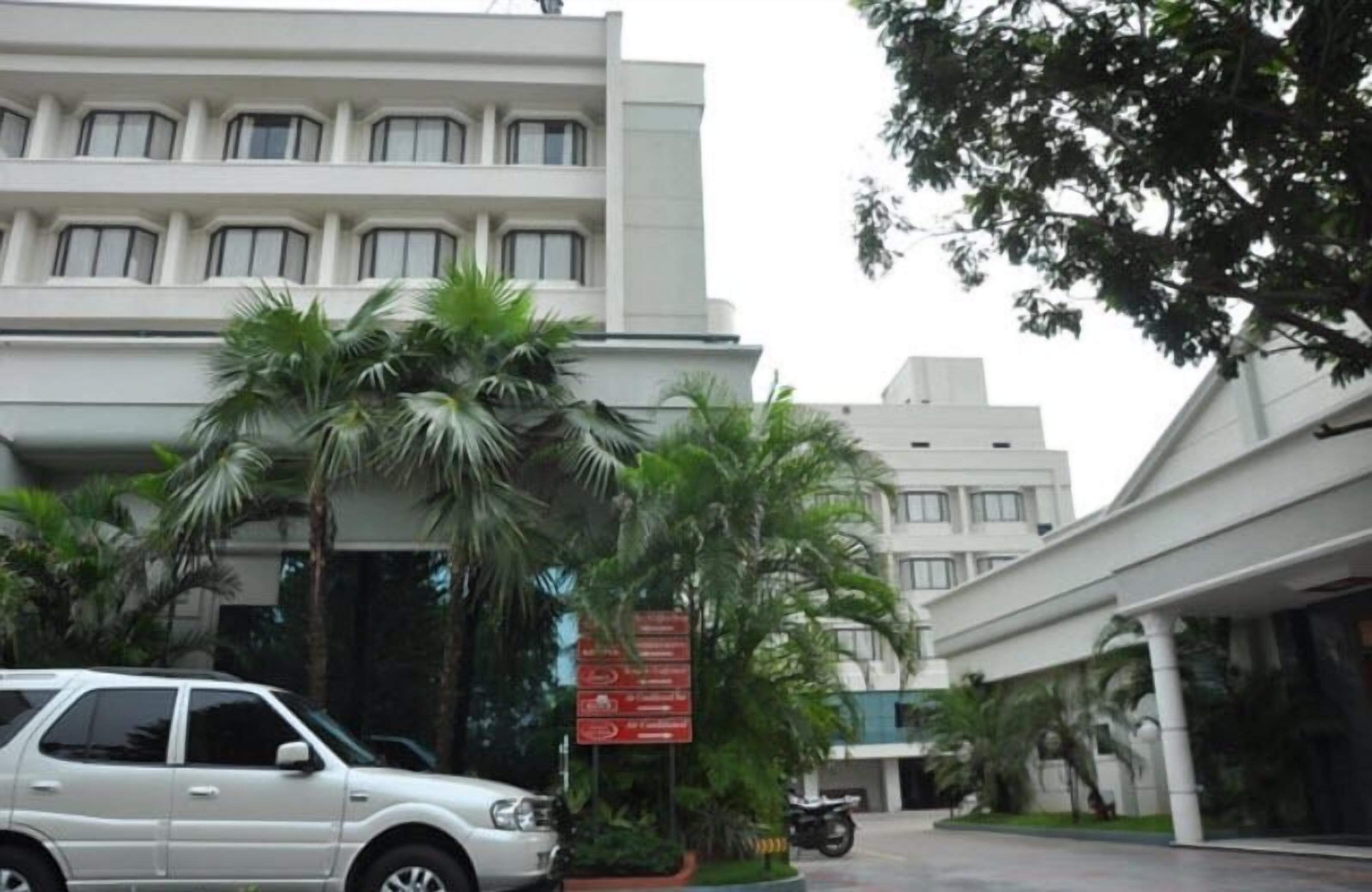 A modern building with a white facade, palm trees, and a parked car.