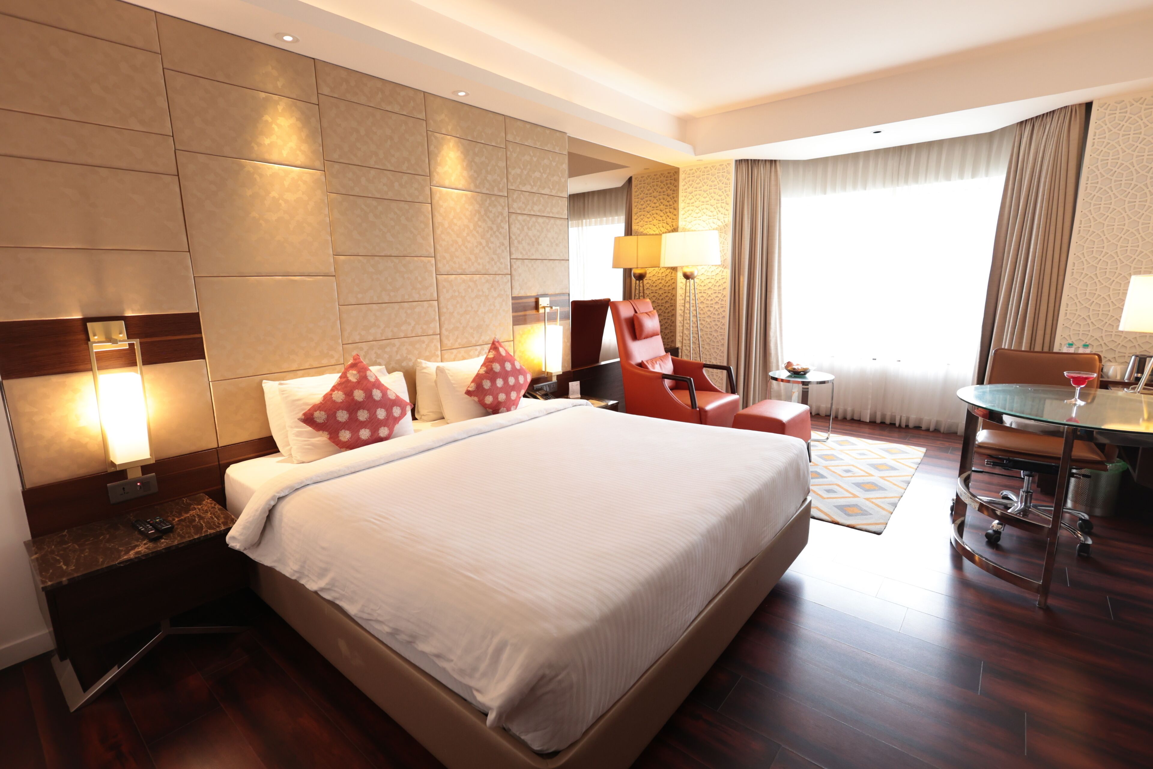 A hotel room with a large bed, a desk, a chair, a lamp, and a window with curtains.