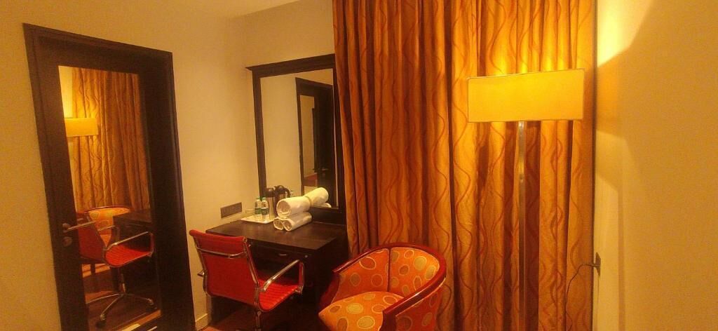 A hotel room with a desk, two chairs, a mirror, and a curtain.