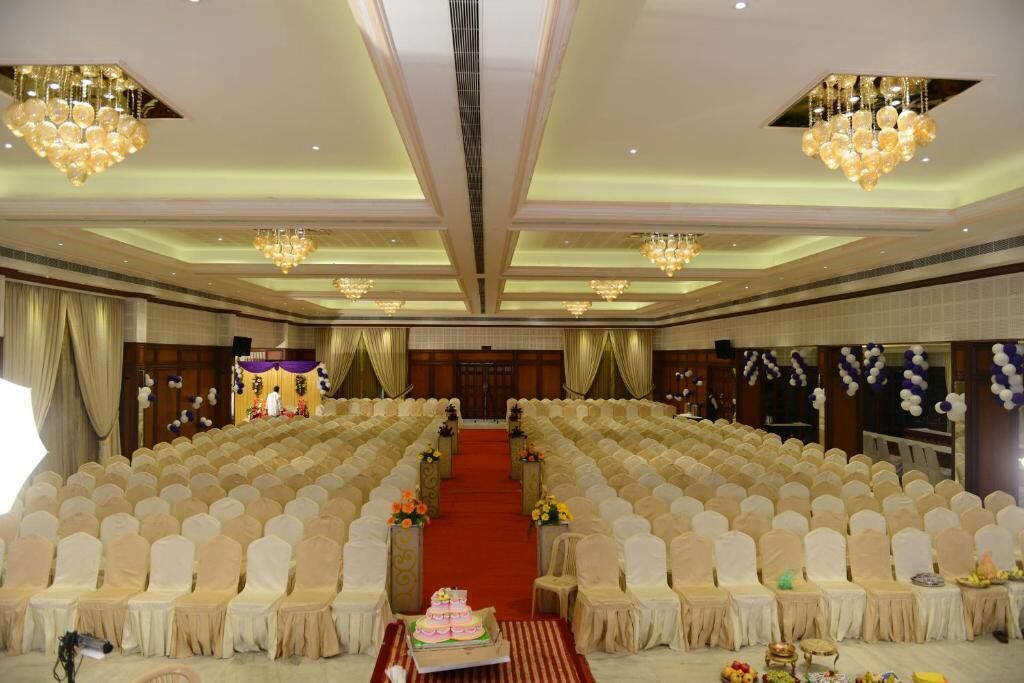 Un salón amplio con filas de sillas blancas, un escenario con alfombra roja y candelabros.