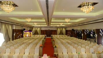 Un salón amplio con filas de sillas blancas, un escenario con alfombra roja y candelabros.