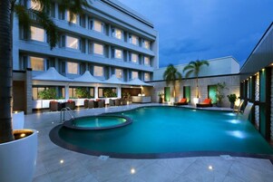Un hotel moderno con piscina, mobiliario exterior y fachada bien iluminada.