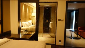 A hotel room with a bed, a sitting area with a table and chairs, a shower area, and a red chair in the corner. - Cenneys Gateway - Pride of Salem (Salem)