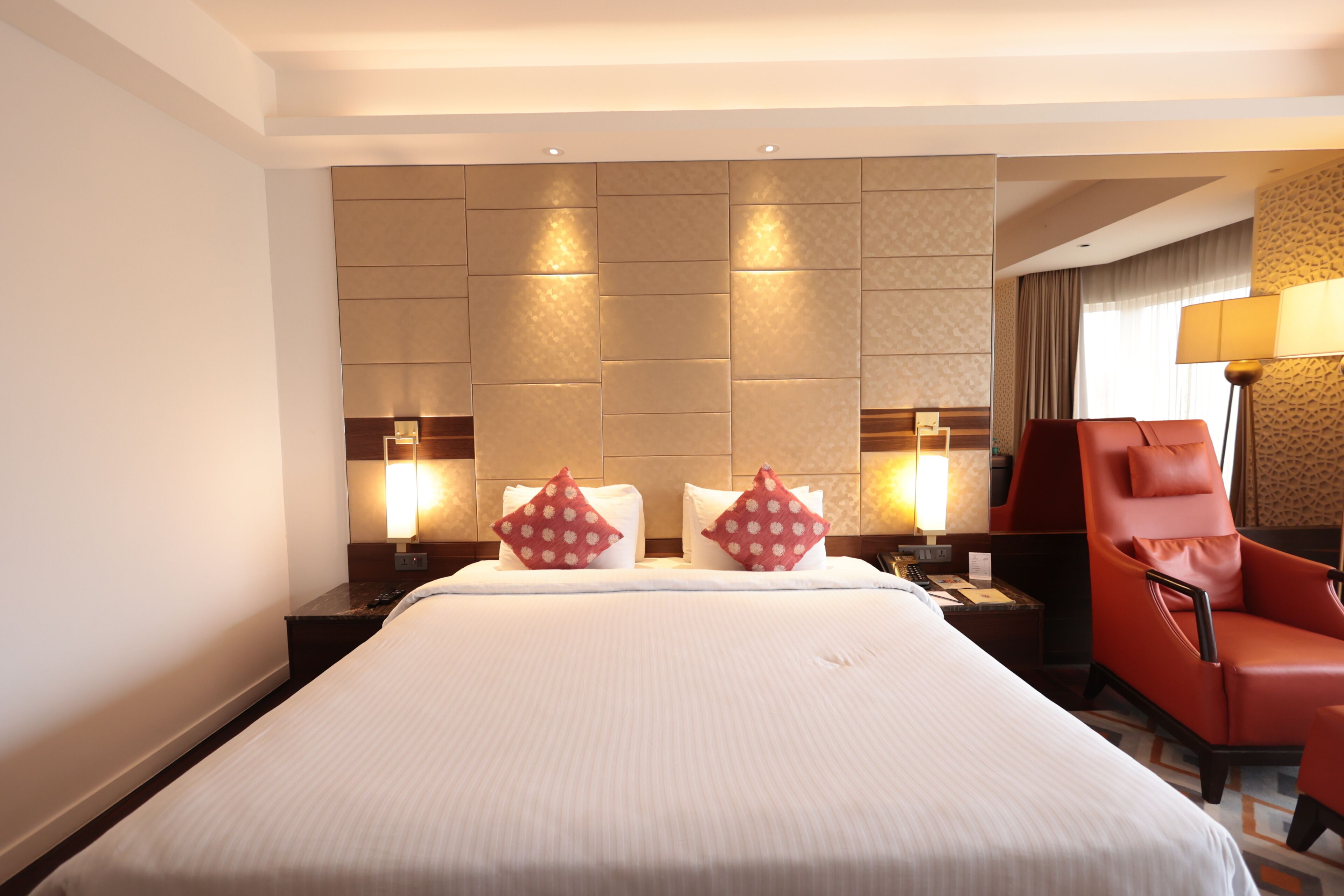 Une chambre d’hôtel avec un grand lit, deux tables de chevet avec des lampes, un fauteuil rouge et un mur à motifs.