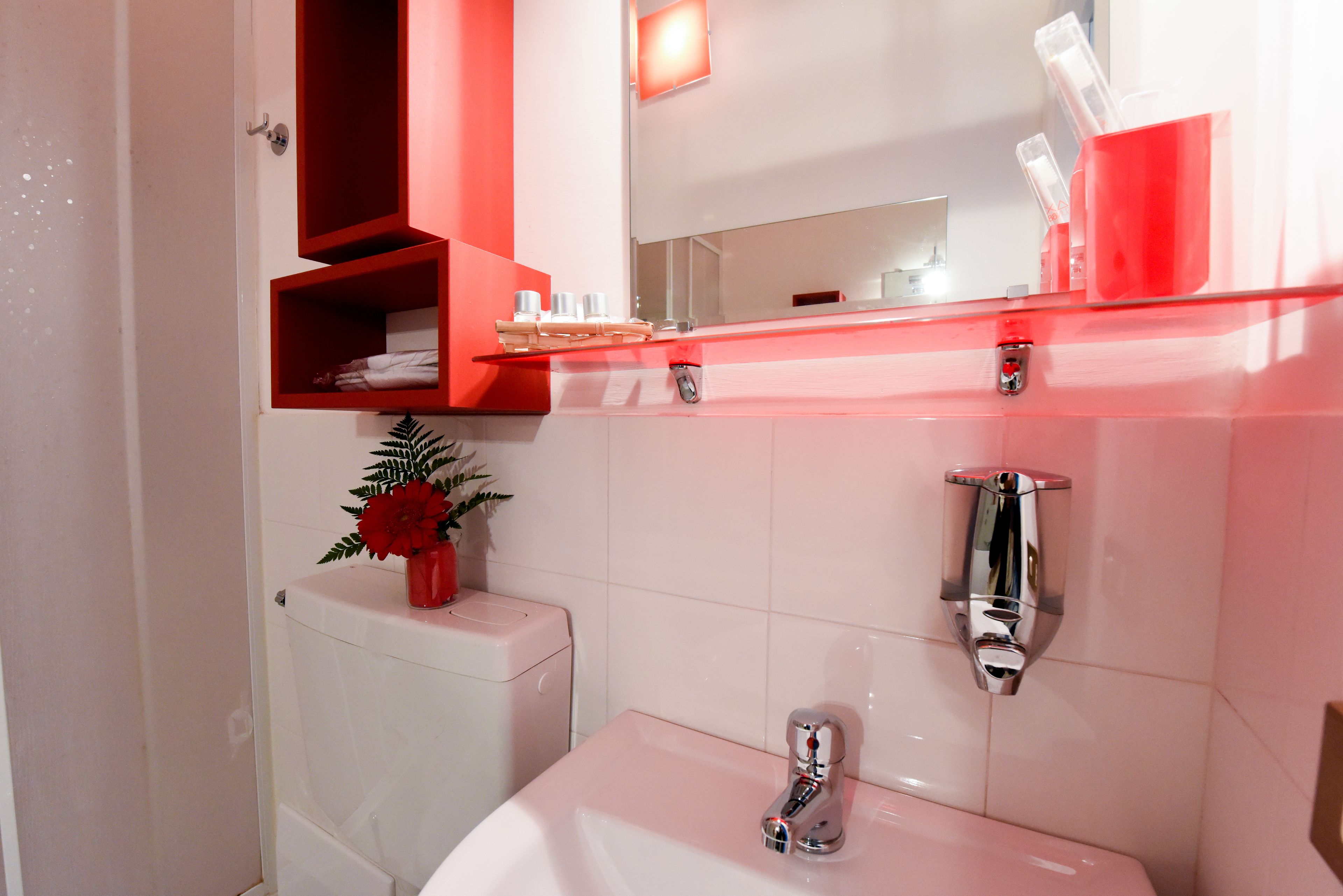 A modern bathroom with a white sink, chrome faucet, and a red-framed mirror above.