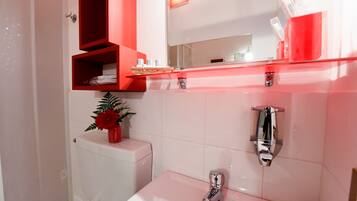 A modern bathroom with a white sink, chrome faucet, and a red-framed mirror above.