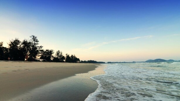 A beach with a clear sky, calm sea, and trees along the shore. - Pantai Regal Hotel (Kuantan)