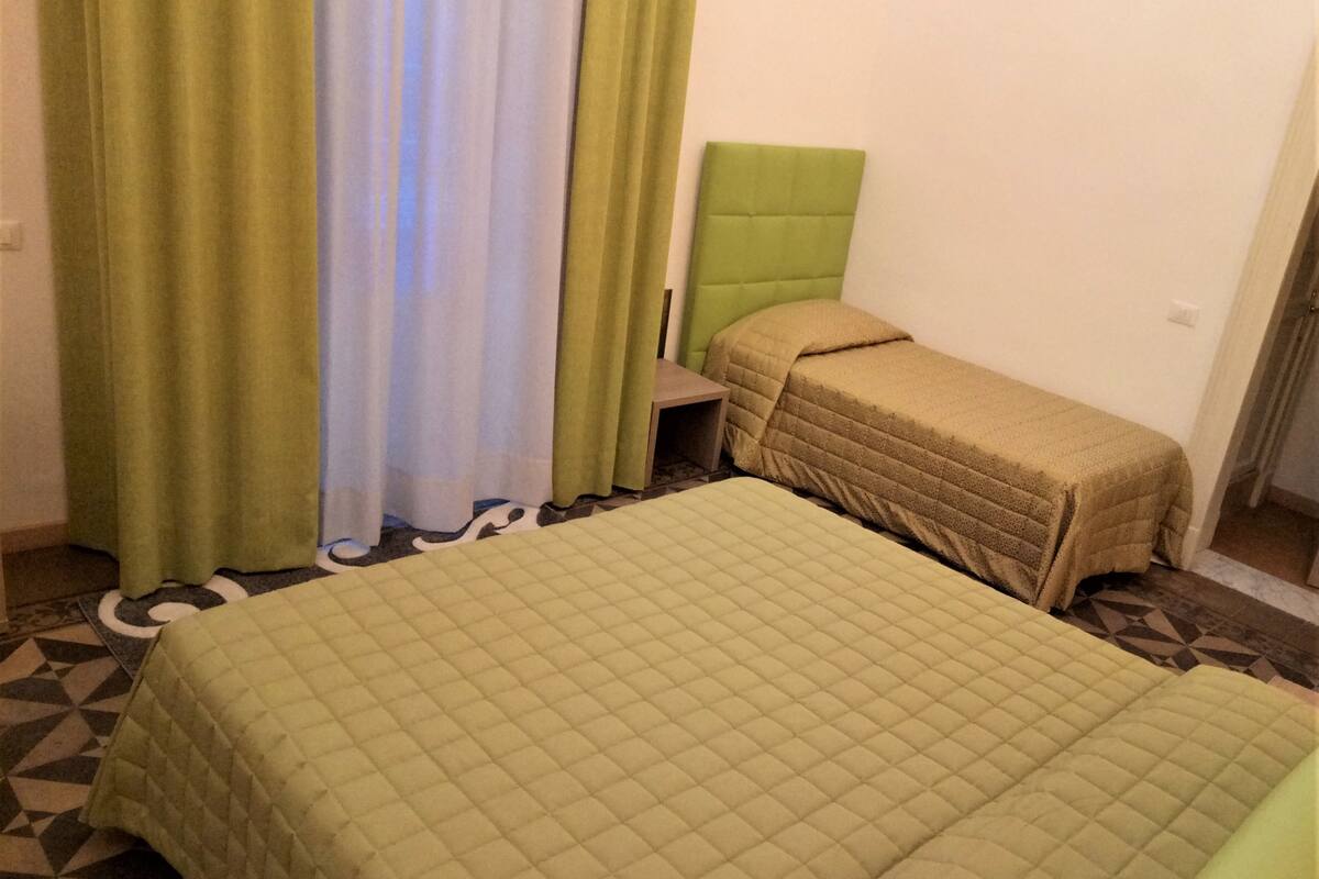 A room with a large bed, a smaller bed, a nightstand, and a green headboard.