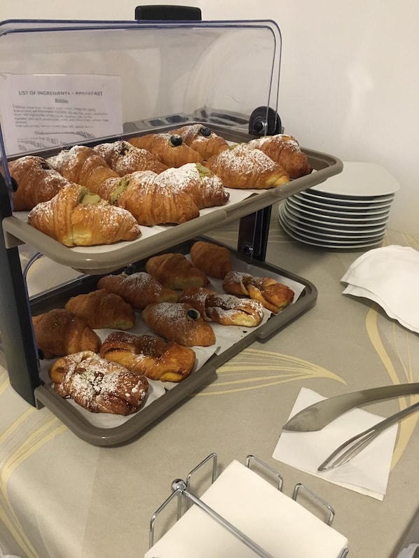 Un buffet de petit-déjeuner proposant diverses pâtisseries, accompagné d’une affiche indiquant les ingrédients.