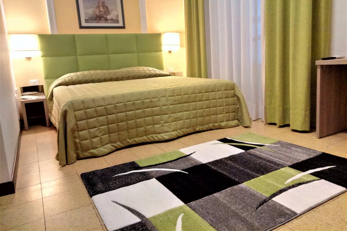 A hotel room with a bed, two bedside lamps, a framed picture on the wall, and a green curtain.