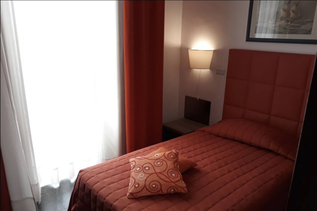A hotel room with a bed, a nightstand, a lamp, and a framed picture on the wall.