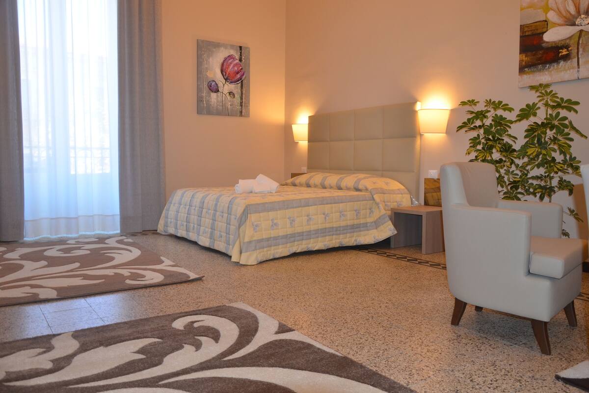 A hotel room with a bed, a chair, a nightstand, a lamp, and a painting on the wall.