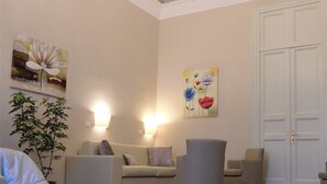 A living room with a beige sofa, two armchairs, a chandelier, and a floral painting on the wall. - Moonlight Hotel & Suites (Catania)