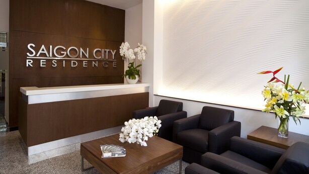 Un espace d’accueil doté d’un comptoir en bois, de sièges noirs et d’une enseigne fixée au mur portant l’inscription « SAIGON CITY RESIDENCE ».