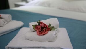 Una cama bien hecha con sábanas blancas y una flor rosa decorativa en el centro.