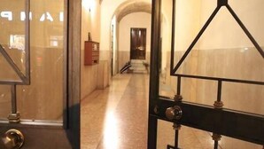 Un pasillo con una puerta de cristal y una verja de metal, que conduce a una habitación con pared de piedra y un armario de madera.