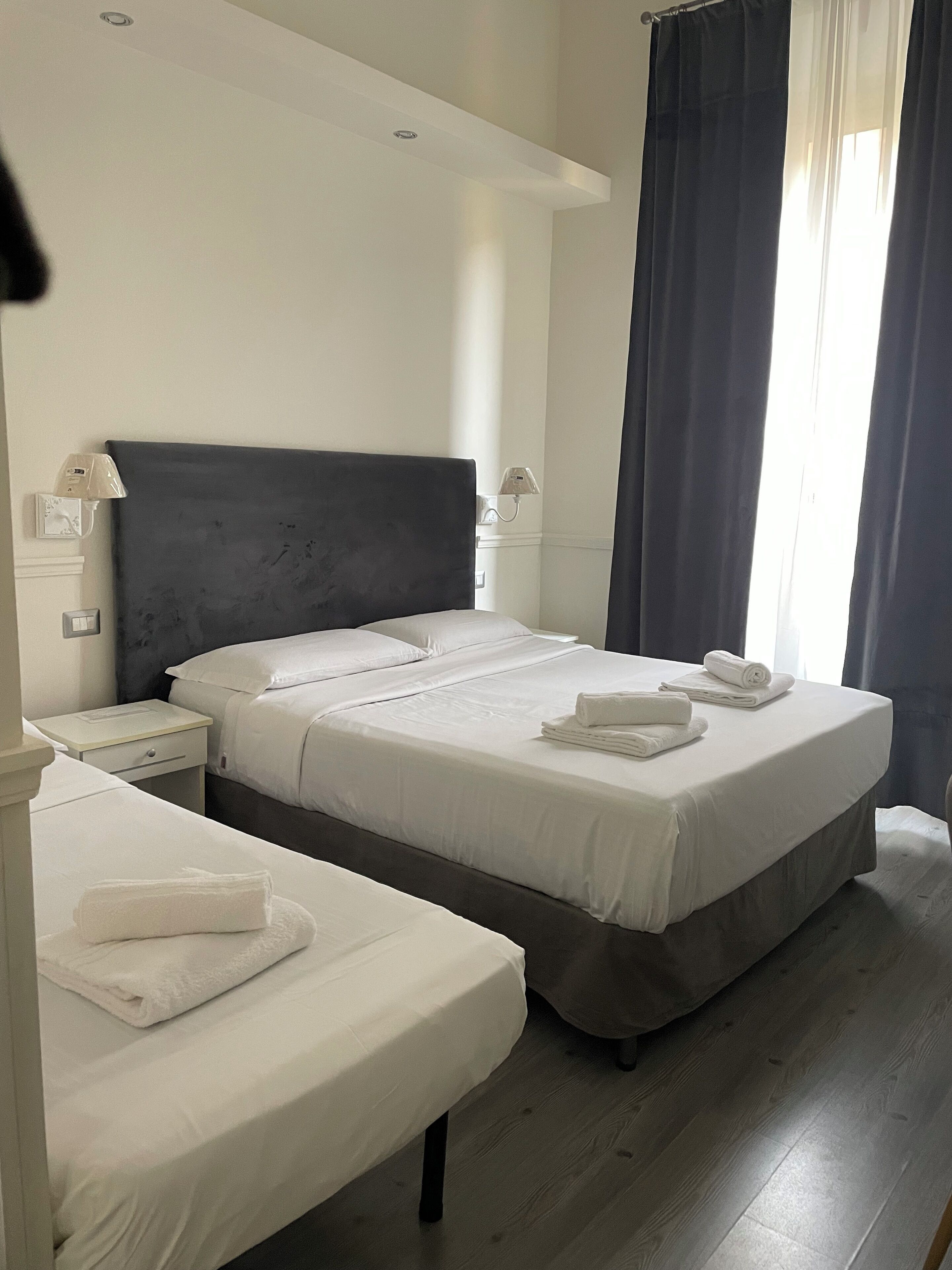 Una camera d'albergo con due letti, un comodino, una lampada e una finestra con tende.