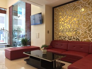 A modern living room with a red sofa, a glass coffee table, and a decorative wall panel. - Golden Lotus Halong Hotel (Bai Chay)