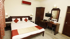A hotel room with a large bed, a desk, a wardrobe, a television, and an air conditioning unit. - Archana Inn (Kanayannur)
