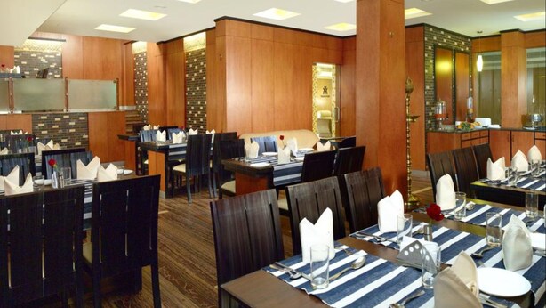A hotel dining area with wooden paneling, striped tablecloths, and neatly set tables. - Archana Inn (Kanayannur)