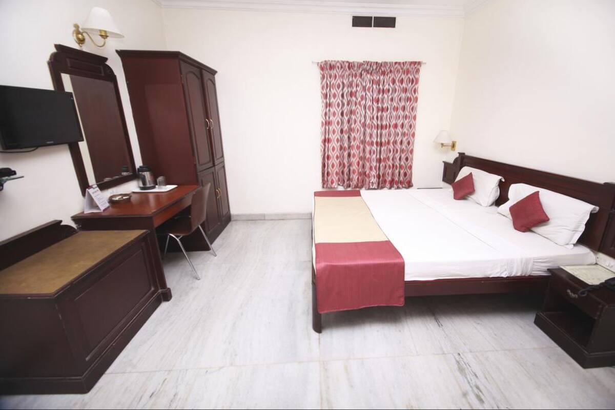 A hotel room with a bed, a desk, a wardrobe, a television, and a window with curtains.