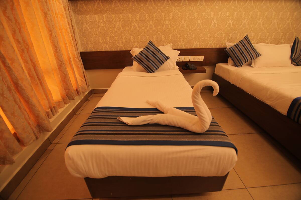 A hotel room with two beds, striped bedding, and a swan-shaped towel on the ottoman.