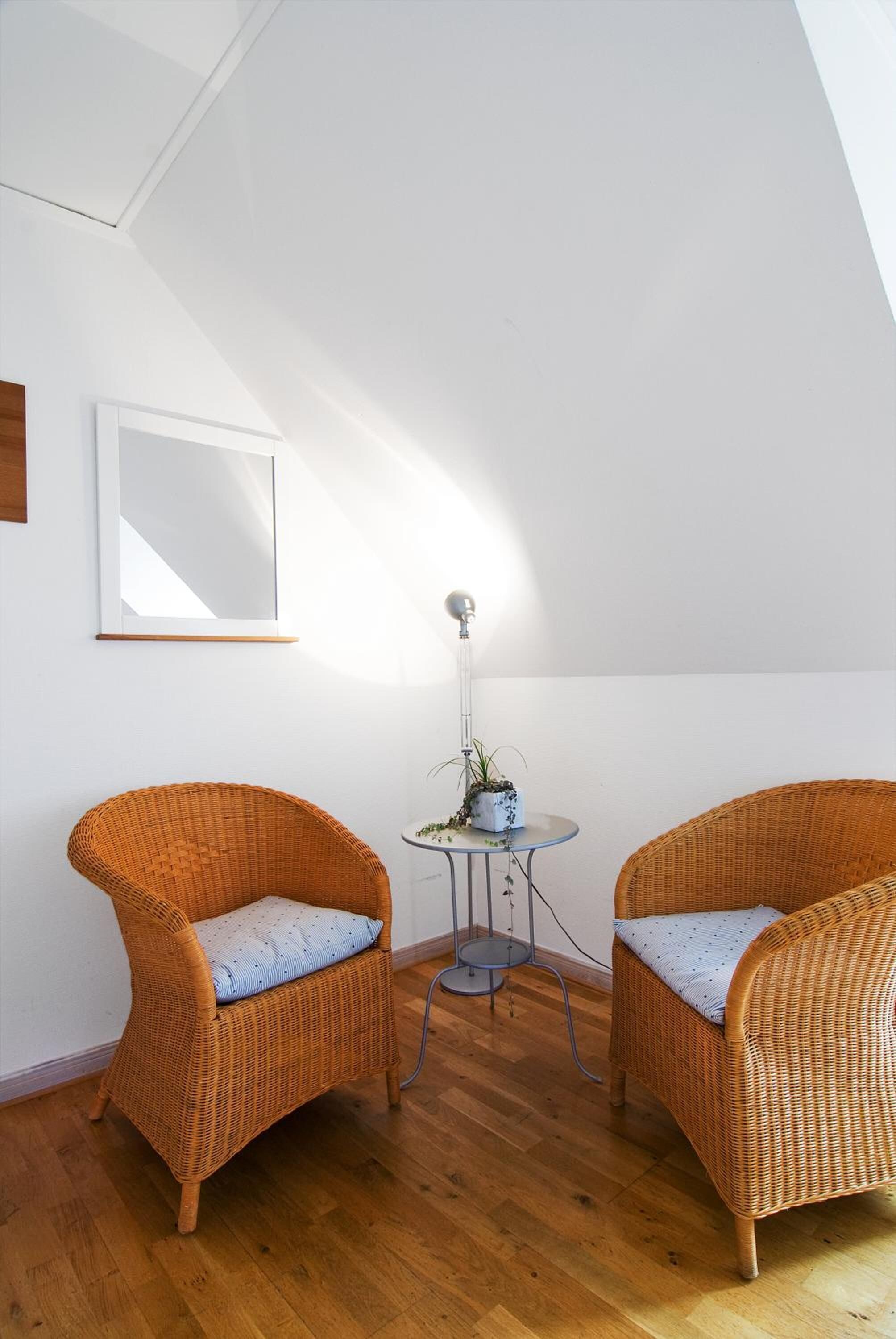 A room with two wicker chairs, a small table with a plant, and a mirror on the wall.