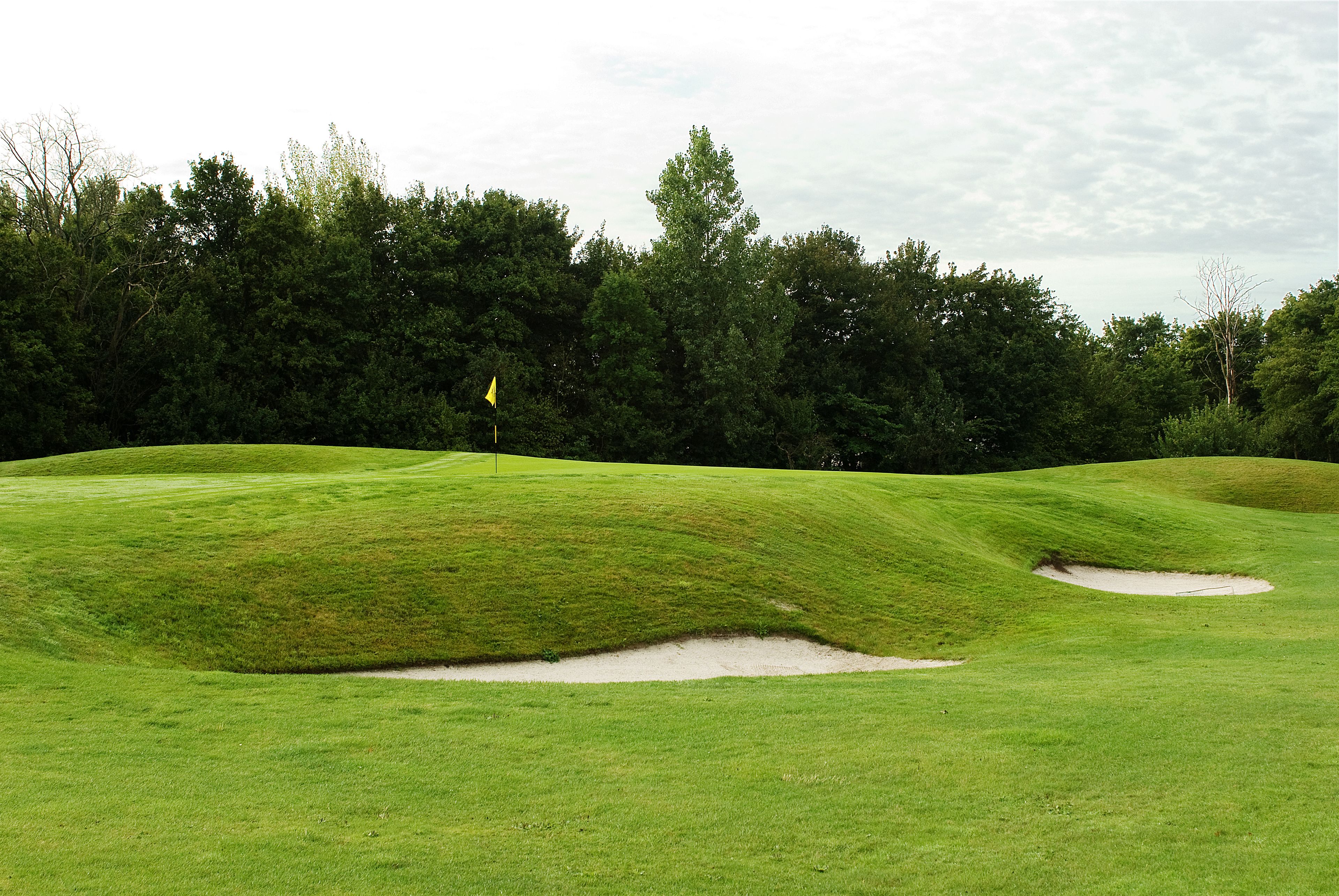 Een golfbaan met verzorgd gras, zandbunkers en een vlag die de hole markeert.