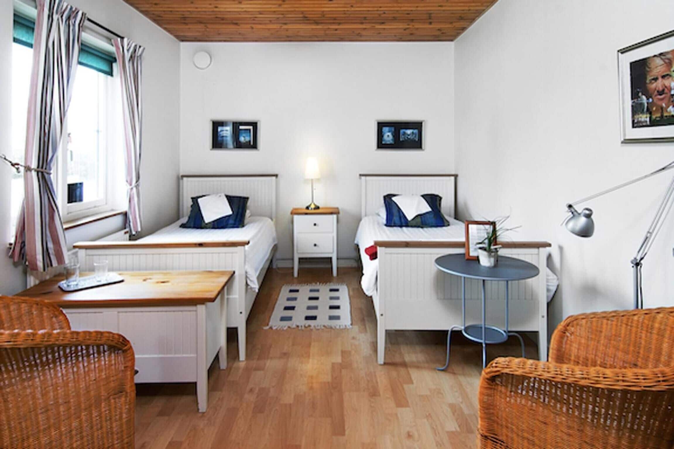 A compact room with two beds, a small table, wicker chairs, and a radiator.