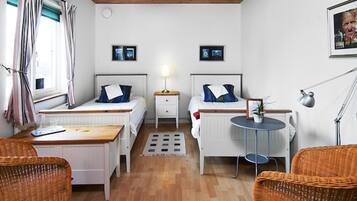A compact room with two beds, a small table, wicker chairs, and a radiator.