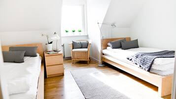 Un dormitorio moderno y bien iluminado con dos camas, una mesita de noche, una silla y una ventana con plantas.