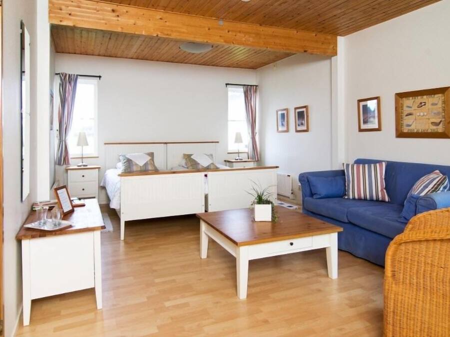 A cozy room with a bed, a blue sofa, a wooden coffee table, and a white dresser.