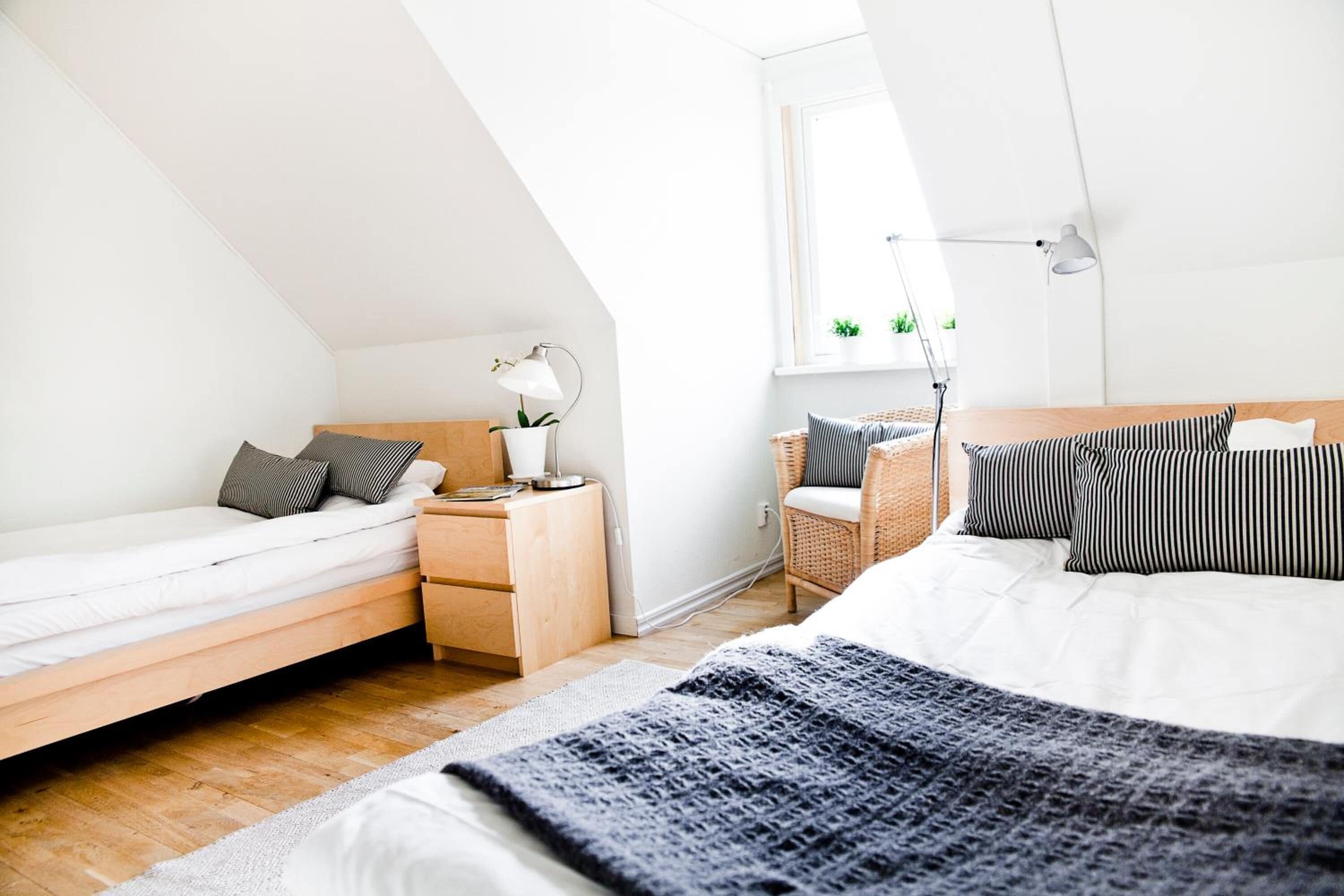 Un dormitorio moderno con cama en altillo, una mesita de noche con lámpara, una pequeña silla y una ventana con plantas.