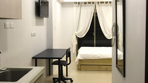 A compact hotel room with a kitchenette, a bed with white curtains, a TV mounted on the wall, and a mirror on the right. - Umali Kayo at Megatower Residences II (Baguio)