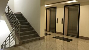 A modern elevator area with a marble floor and a metal staircase. - Umali Kayo at Megatower Residences II (Baguio)