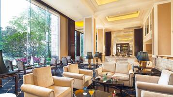 A spacious lobby with multiple seating areas, a bar, and large windows offering a view of the outdoors.