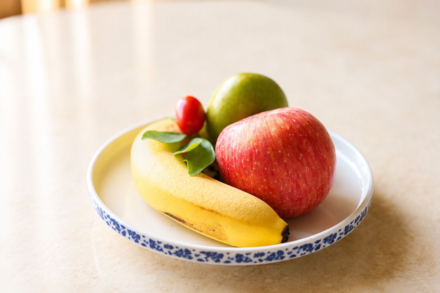 A plate with a banana, an apple, and a cherry on a table.