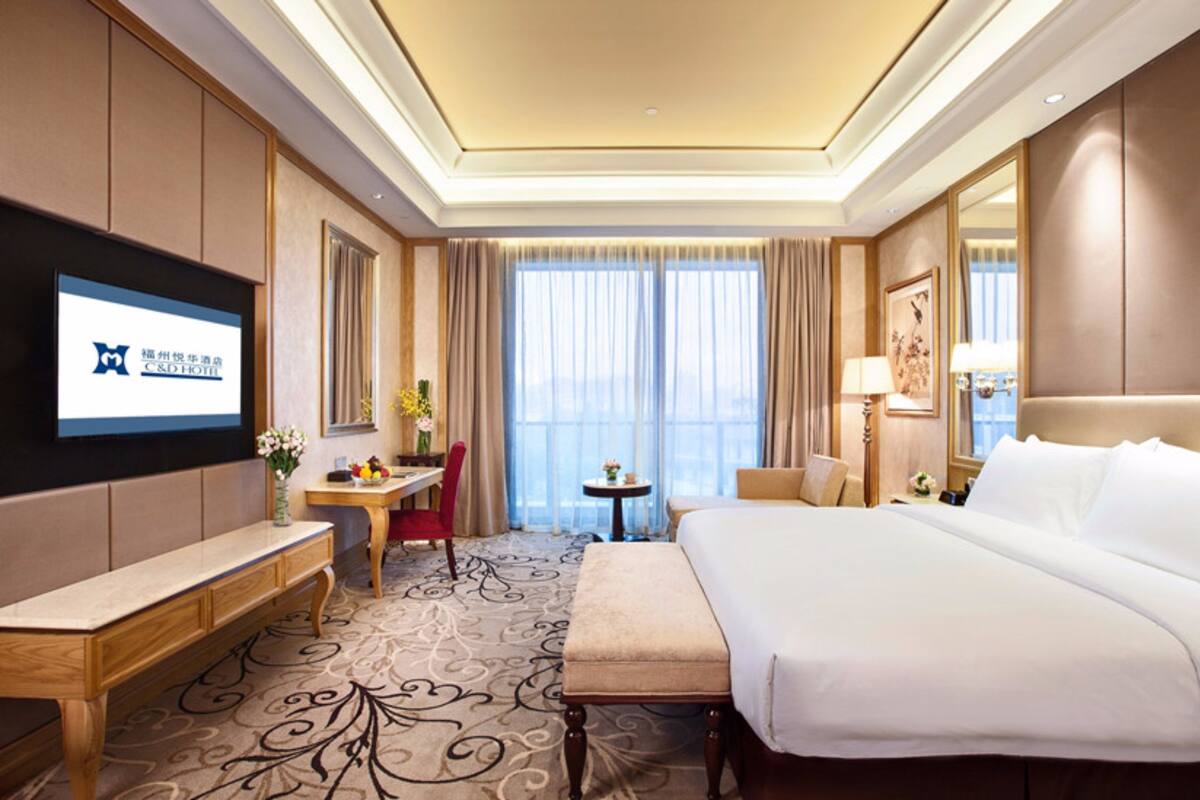 A hotel room with a large bed, a desk, a chair, a small table, and a TV on the wall.
