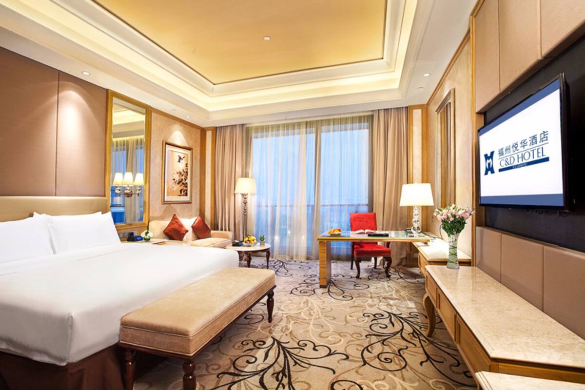 A hotel room with a large bed, a desk, a TV, and a view of the city.