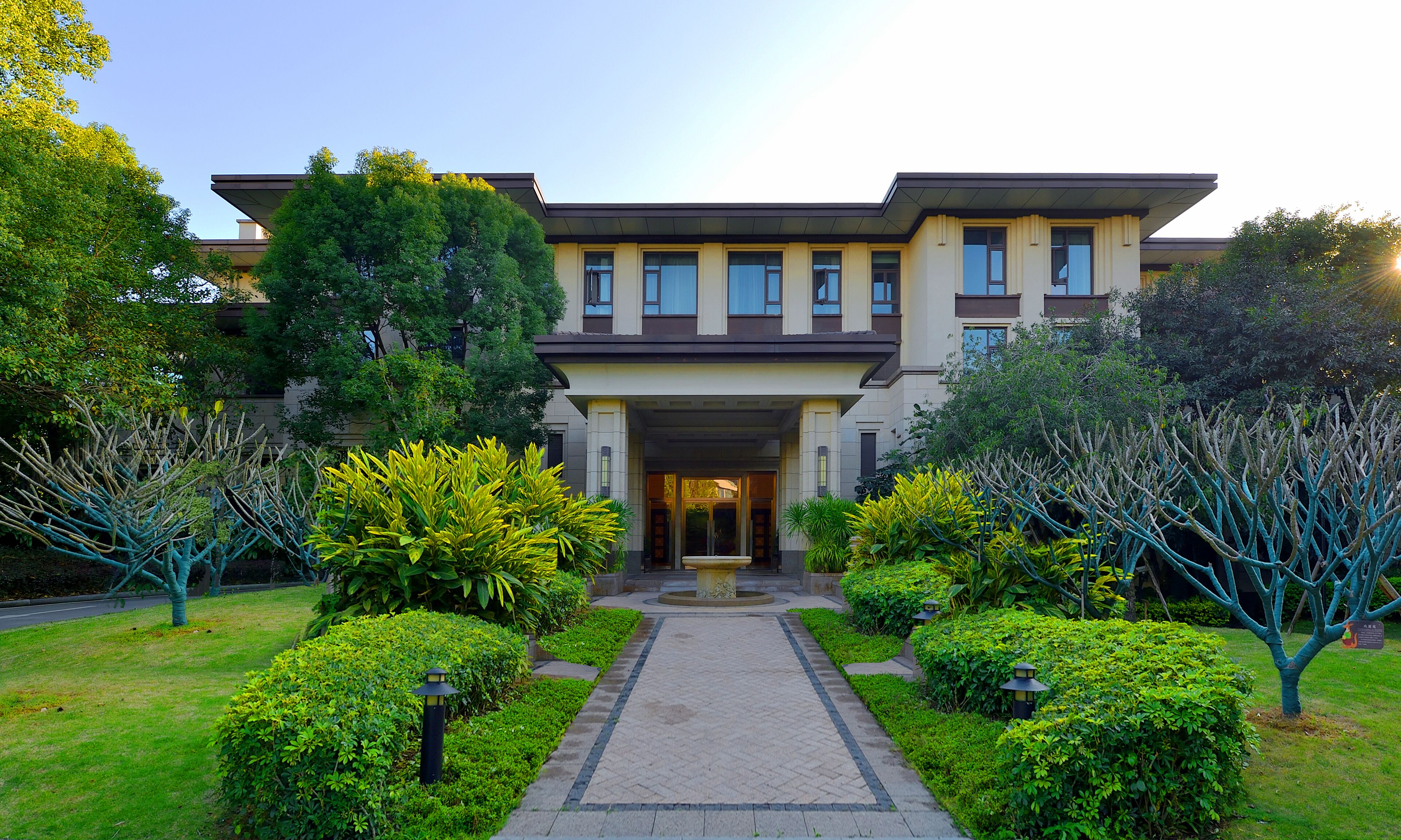 A modern two-story building with a symmetrical facade, a central entrance, and a well-maintained garden with trimmed bushes and trees.