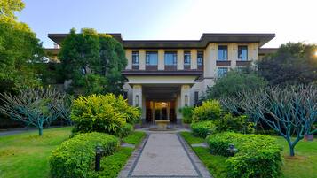 A modern two-story building with a symmetrical facade, a central entrance, and a well-maintained garden with trimmed bushes and trees.