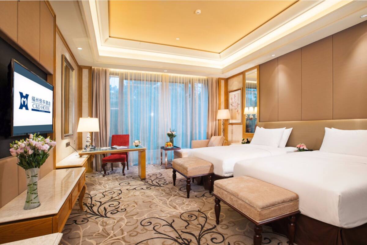 A hotel room with two beds, a desk, a chair, and a TV.