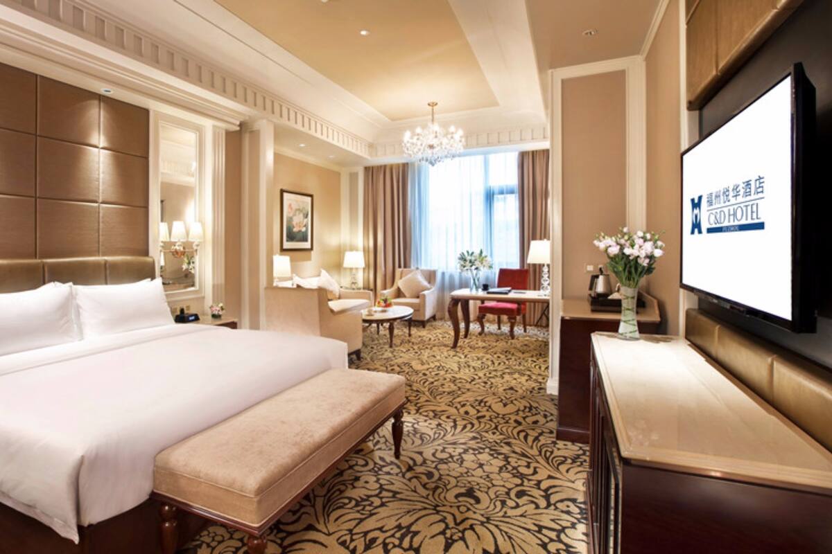 A hotel room with a large bed, a desk, a chair, a television, and a chandelier.