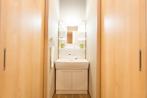 A narrow hallway with a white sink and mirror, wooden doors, and a small window. - Group STAY CLASSE 01 (Osaka)