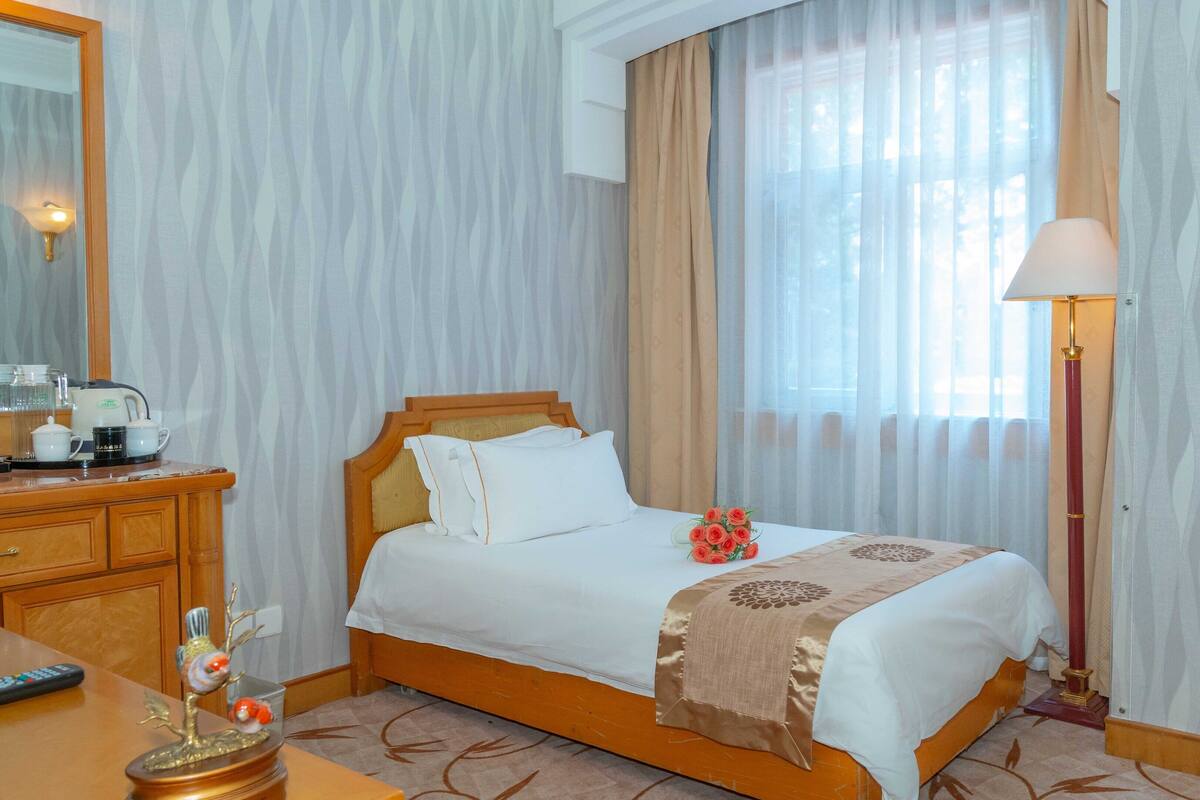 Una habitación de hotel con una cama, una mesita de noche con lámpara, un aparador y un espejo.