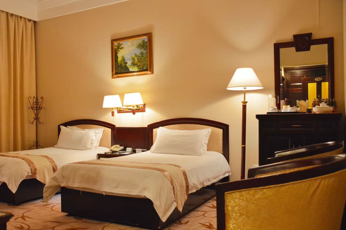 Una habitación de hotel con dos camas, un cuadro en la pared, una lámpara y un espejo.